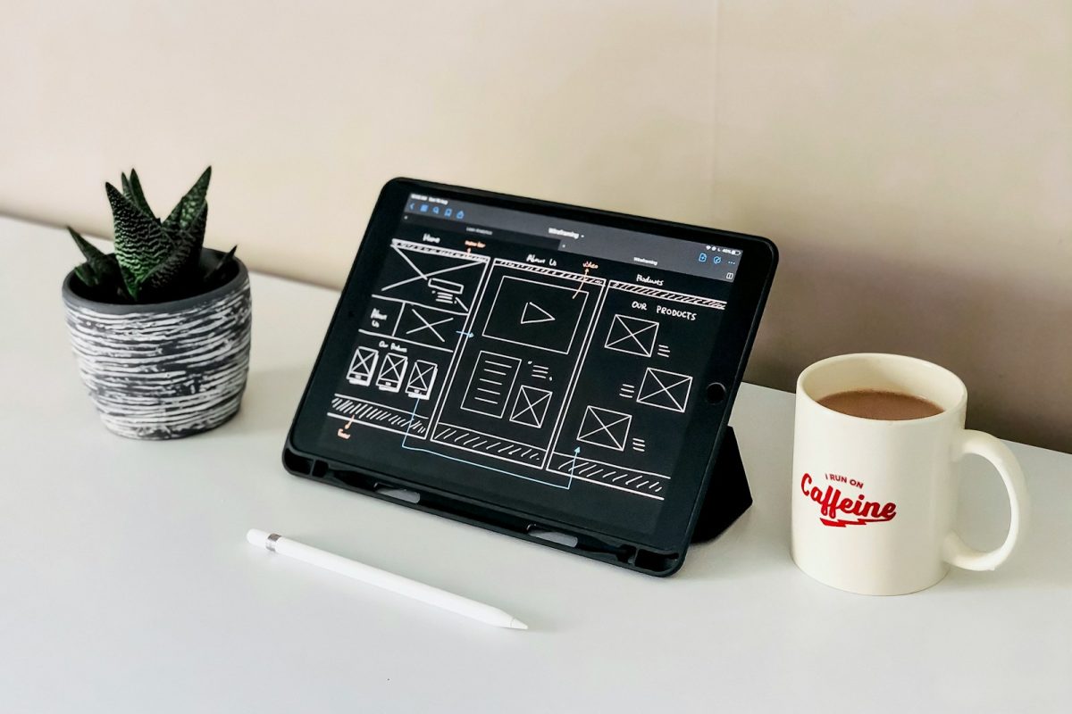 black ipad beside white ceramic mug on white table